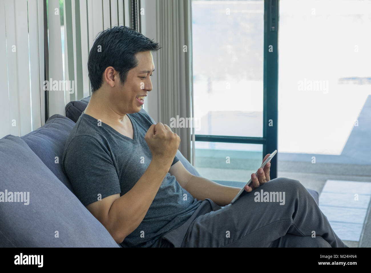 Homme assis sur un canapé et regarder un match de football en direct en streaming sur tablette et jusqu'à bras pour boire de l'équipe.sport digital lifestyle Banque D'Images