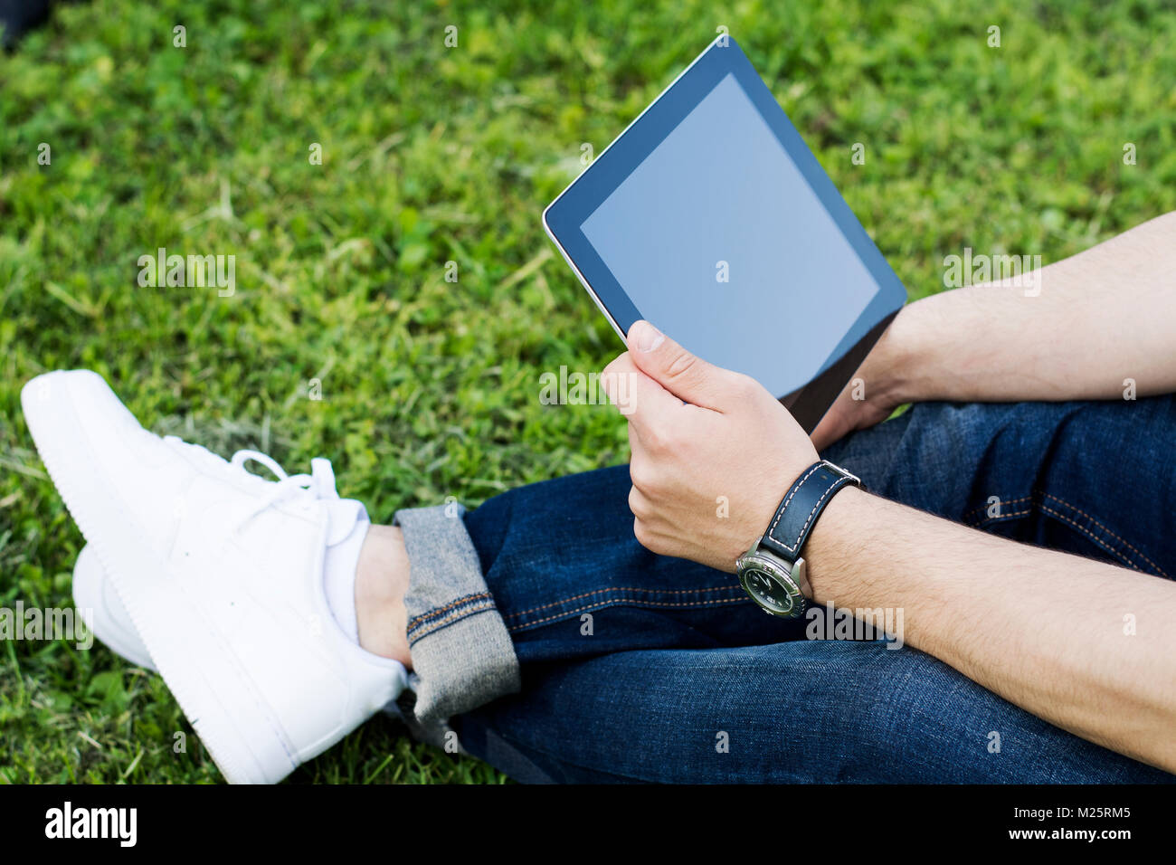 Jeune homme avec tablet sitting in university Park, à la recherche à l'écran. Banque D'Images