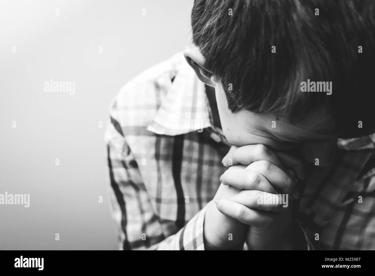 Un jeune garçon avec sa tête baissée dans la prière. Banque D'Images