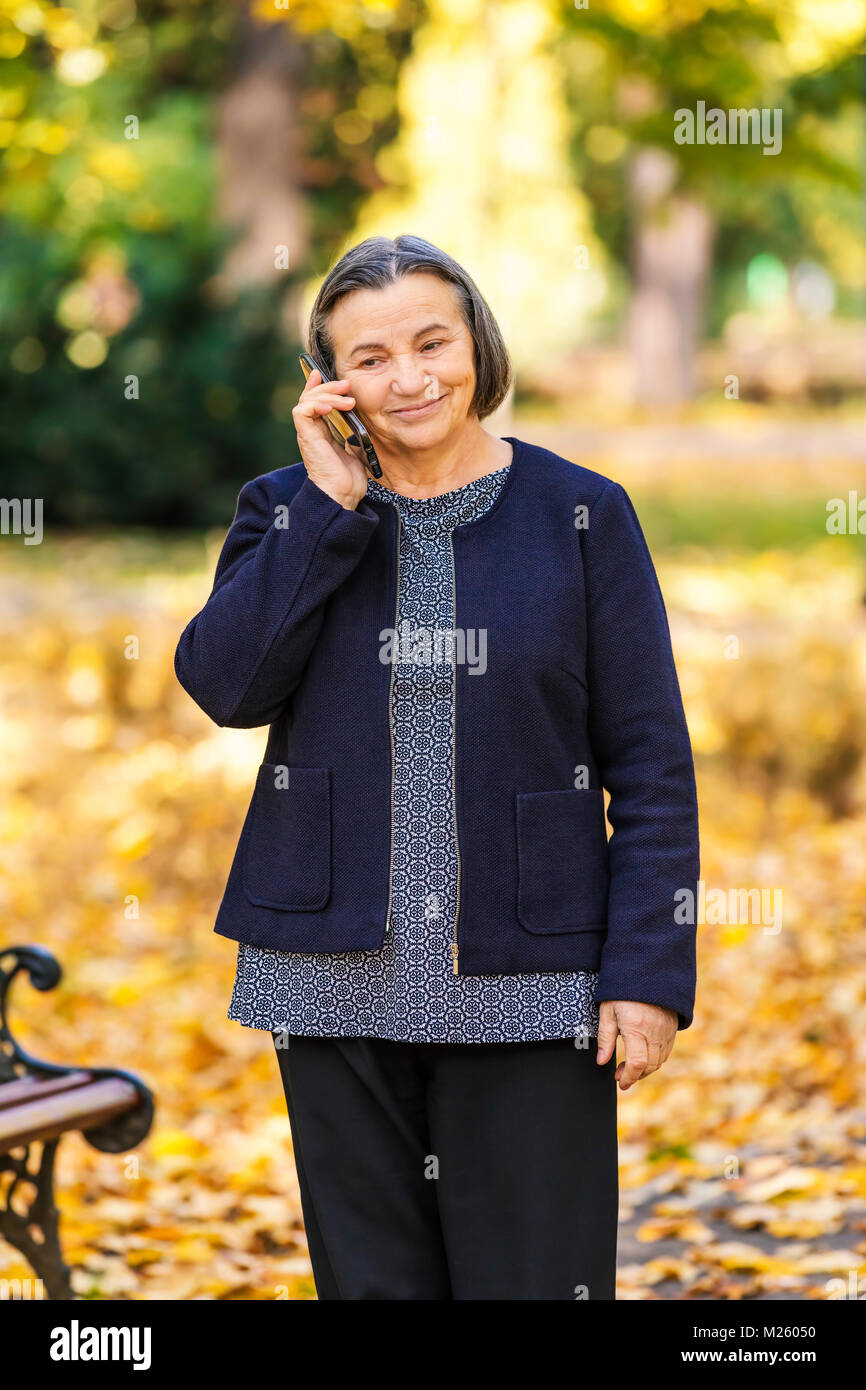 Senior Positive Woman talking on smartphone outdoors in park. Banque D'Images