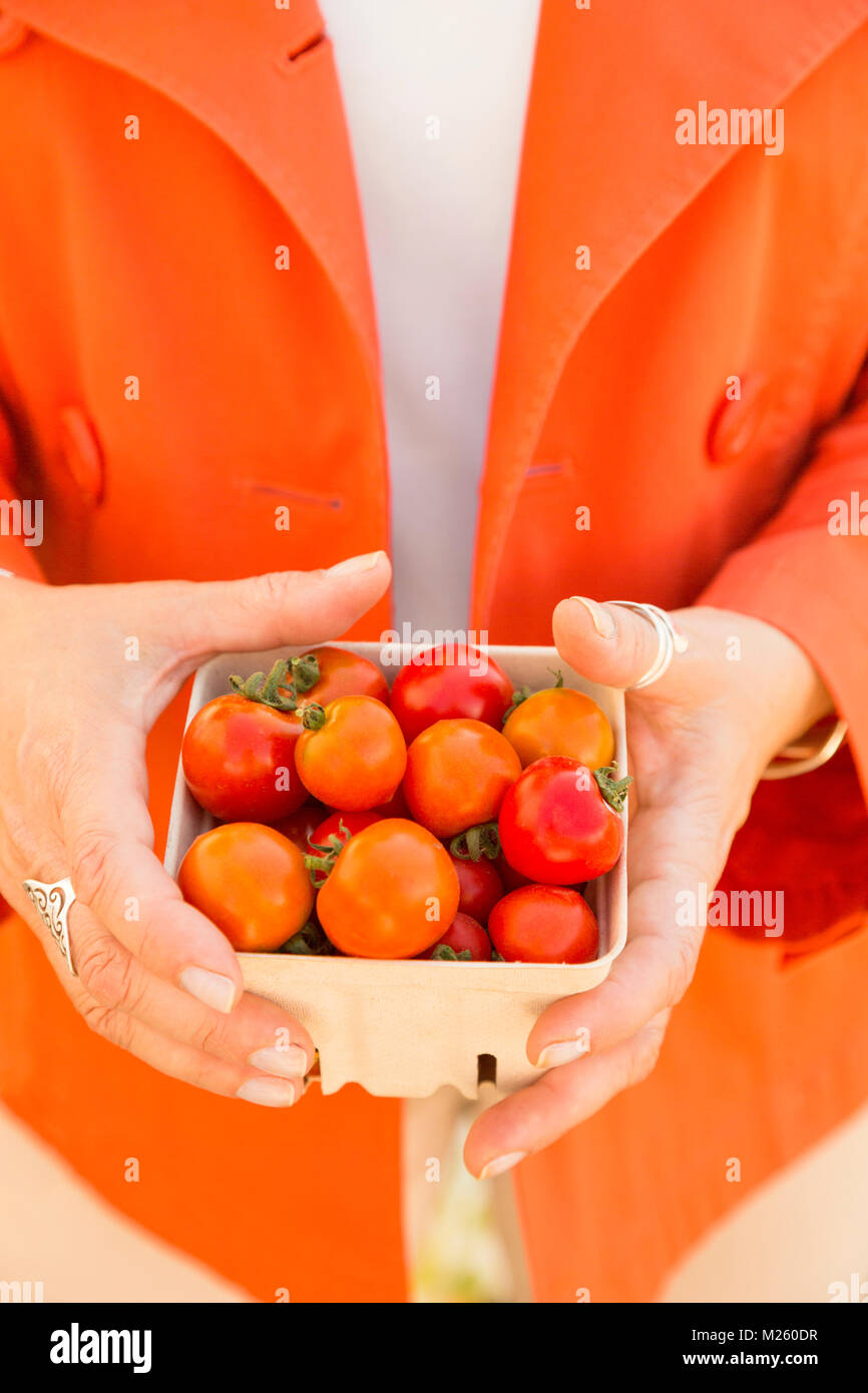 Shopping pour les légumes frais produits à un marché de producteurs. Close up of hands holding a glass panier contenant avec tomates cerises biologiques mûrs. Banque D'Images