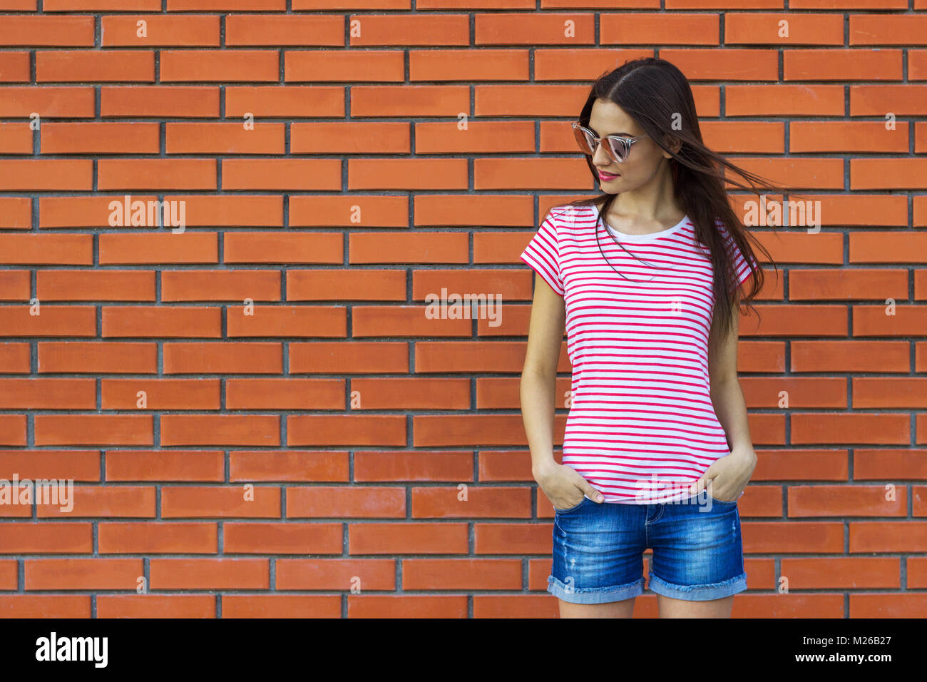 Hipster girl porter du rouge et blanc rayé t-shirt, lunettes de soleil et  la mode short jeans posant contre un mur en brique, d'arrière-plan street  style minimaliste Photo Stock - Alamy