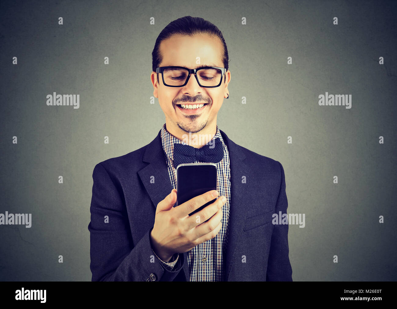 Bel homme élégant en nœud papillon et des lunettes smartphone navigation et souriant, heureux. Banque D'Images