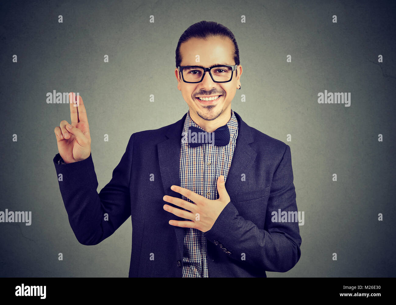 Jeune homme élégant en lunettes holding hand sur la poitrine et de donner une promesse heureusement. Banque D'Images