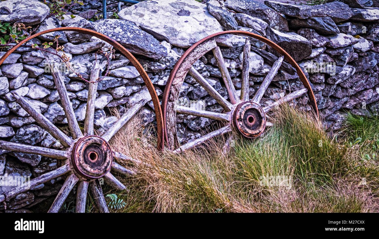 Ancienne paire de roues de chariot en décomposition, appuyé contre un mur de pierre Banque D'Images