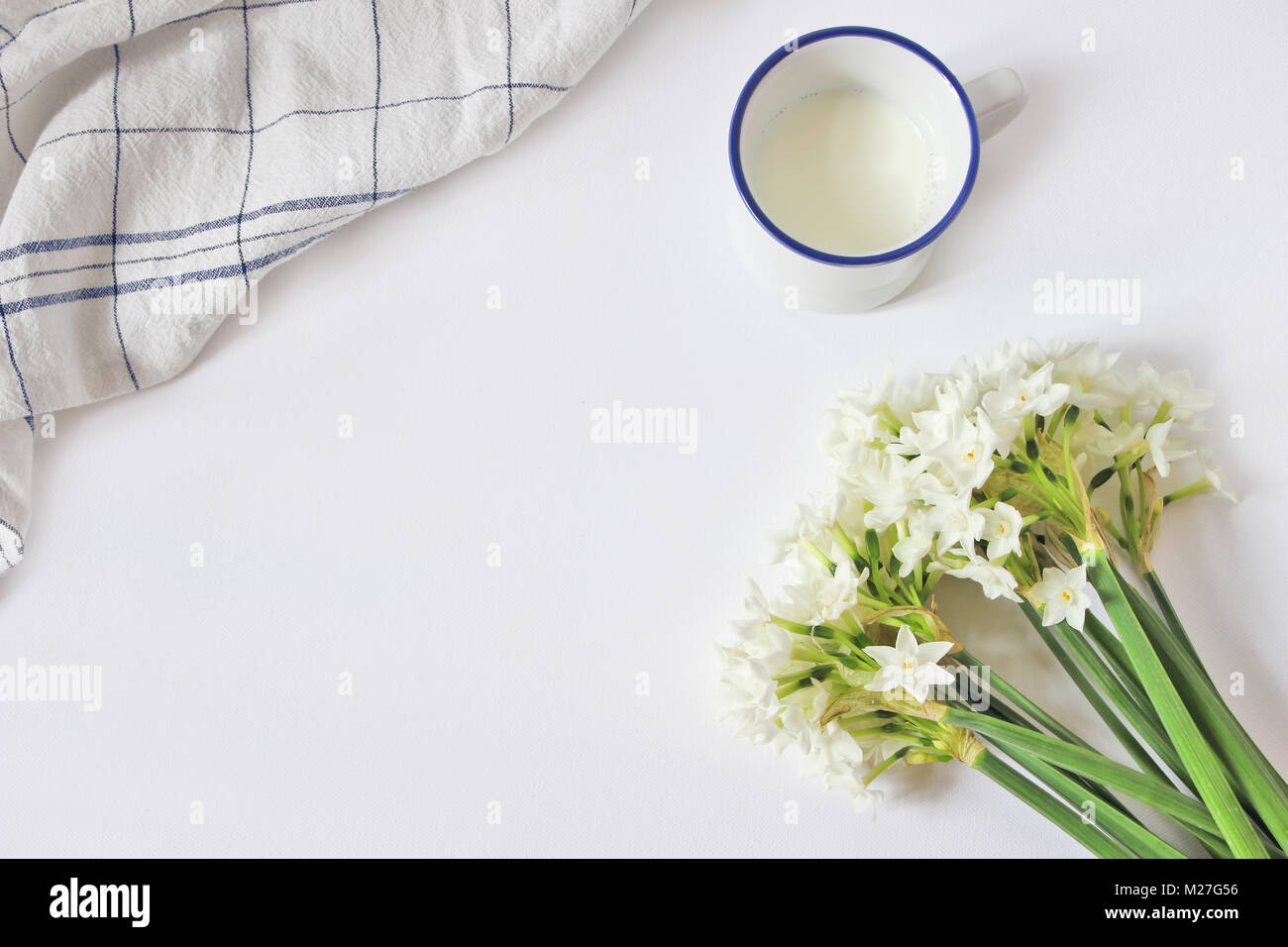 Scène de petit-déjeuner avec mug de lait, serviette et bouquet de NARCISSE, JONQUILLE fleurs sur fond de table blanc. Composition de printemps, Pâques concept. Mise à plat, vue du dessus. Image Style. Banque D'Images