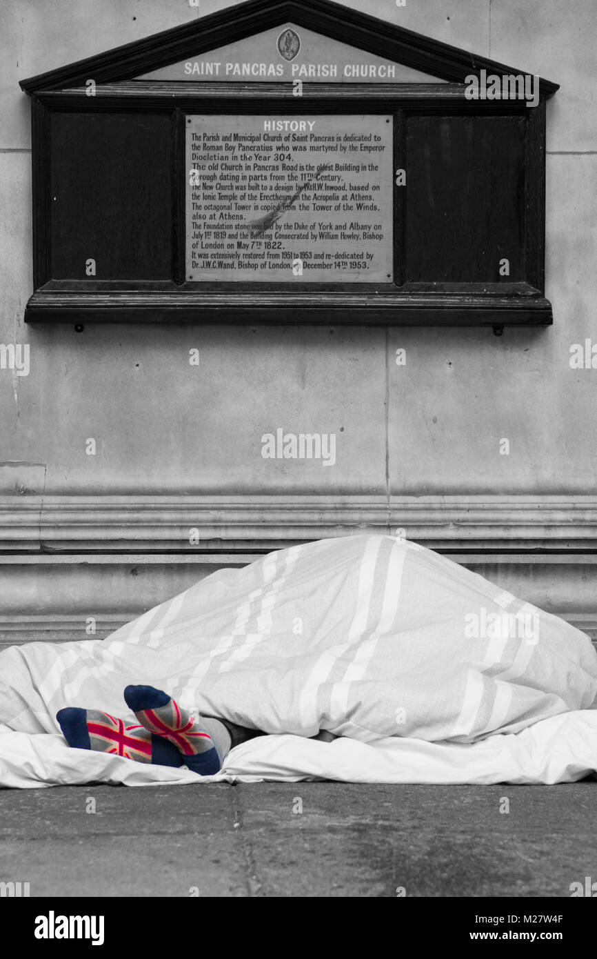 Vue panoramique tourné de sans-abri patriotique afficher ses chaussettes Union Jack dormir sous un abri de porte de l'église éléments de lui dans le centre de Londres. Banque D'Images