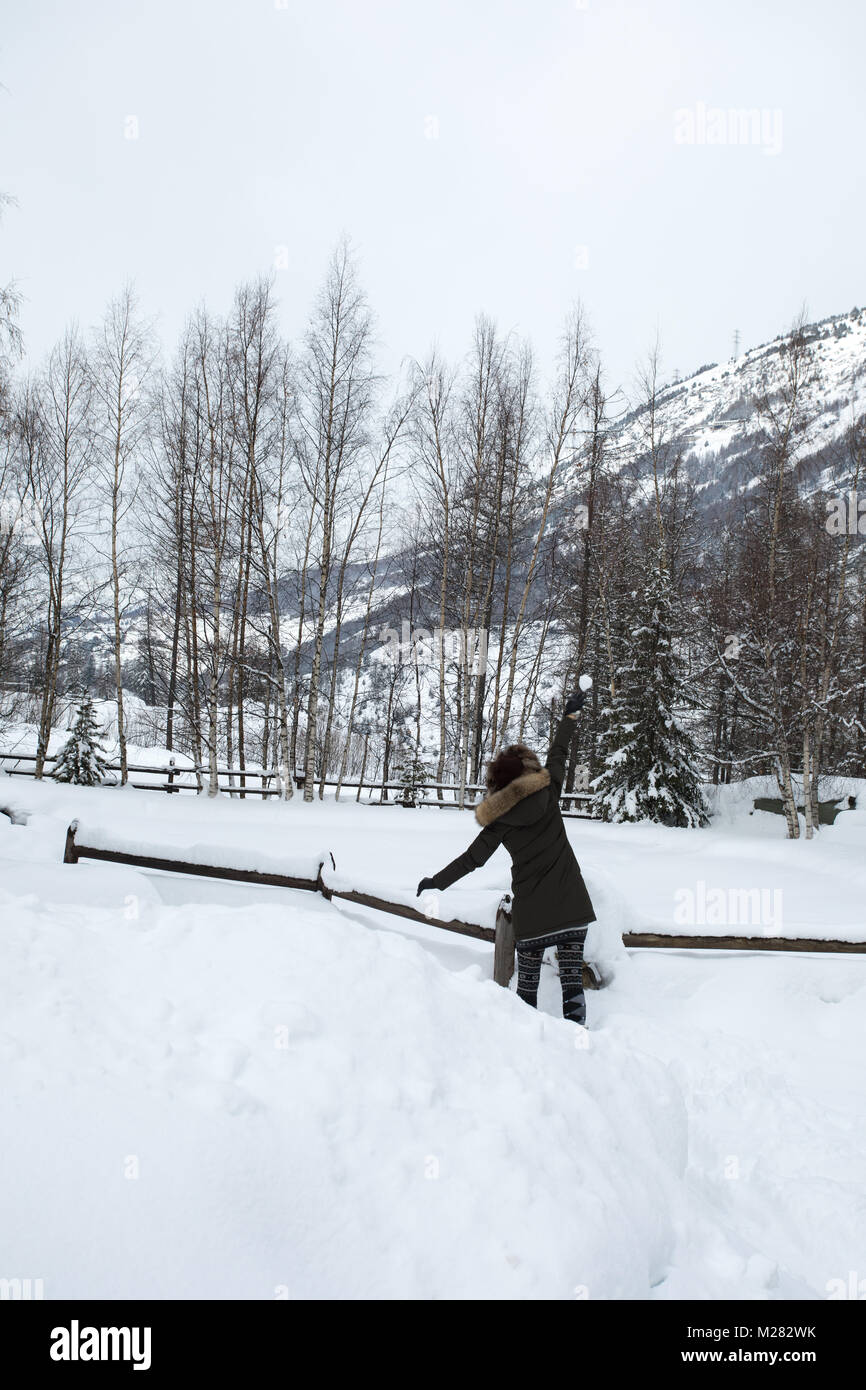 Dos de fille blonde, porter de la hat et parka de fourrure, la marche sur la neige, avec forêt arbre nu en hiver, et jetant des boules de neige. Banque D'Images