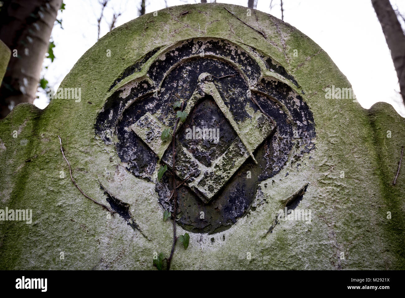 Une pierre tombale maçonnique à Tower Hamlets Cemetery avec la signature du franc-maçon square et gravée à l'emblème de la boussole en décomposition lentement en pierre. Banque D'Images
