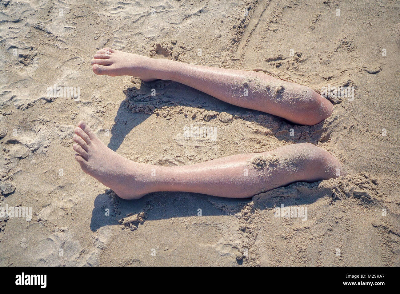 Les jambes d'un garçon enterré dans le sable d'une plage, de style vintage Banque D'Images