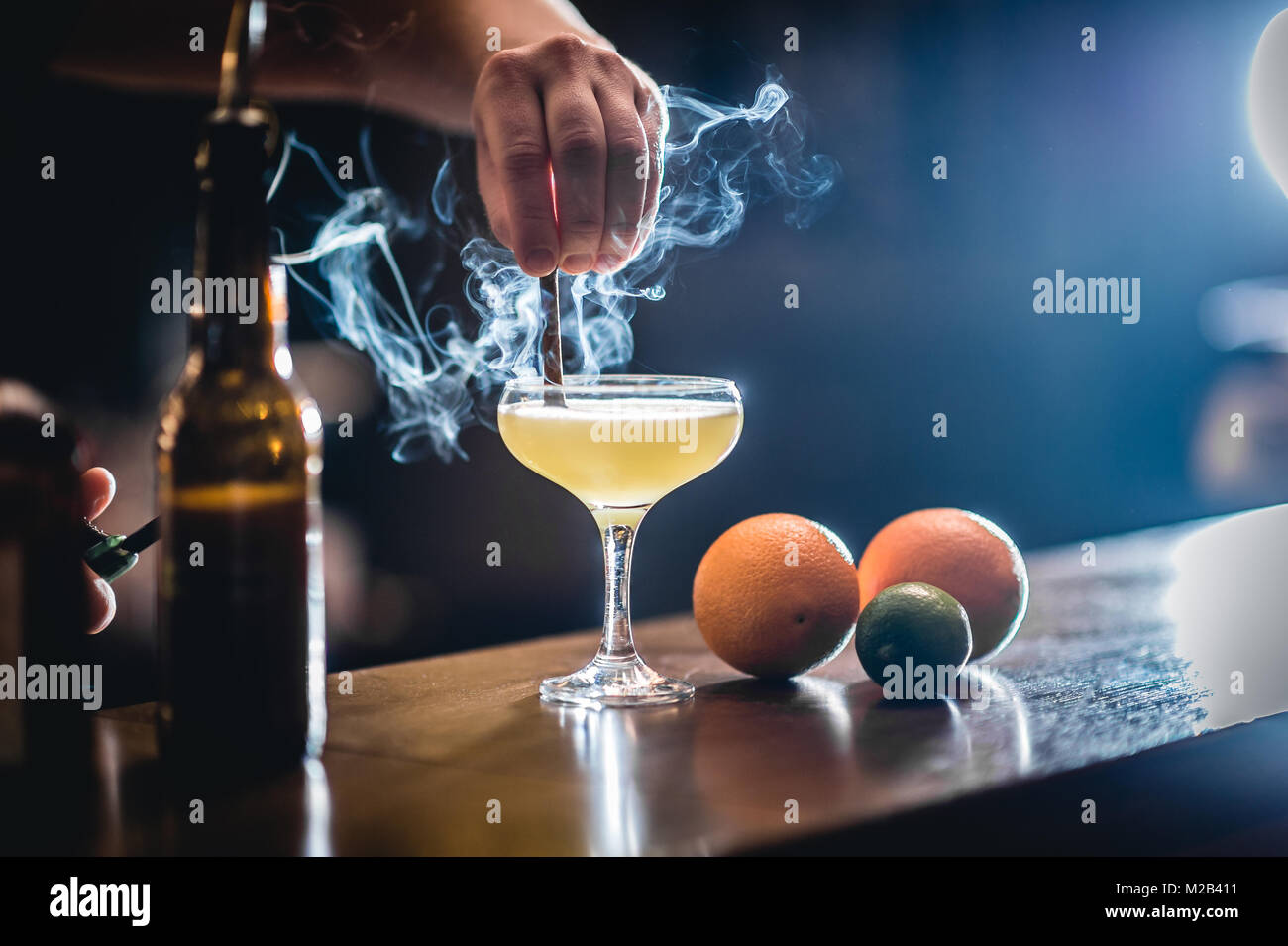 L'alcool dans le verre à cocktail avec de la fumée et cinemon coller l'arrière-plan flou. Verre au bar. Banque D'Images