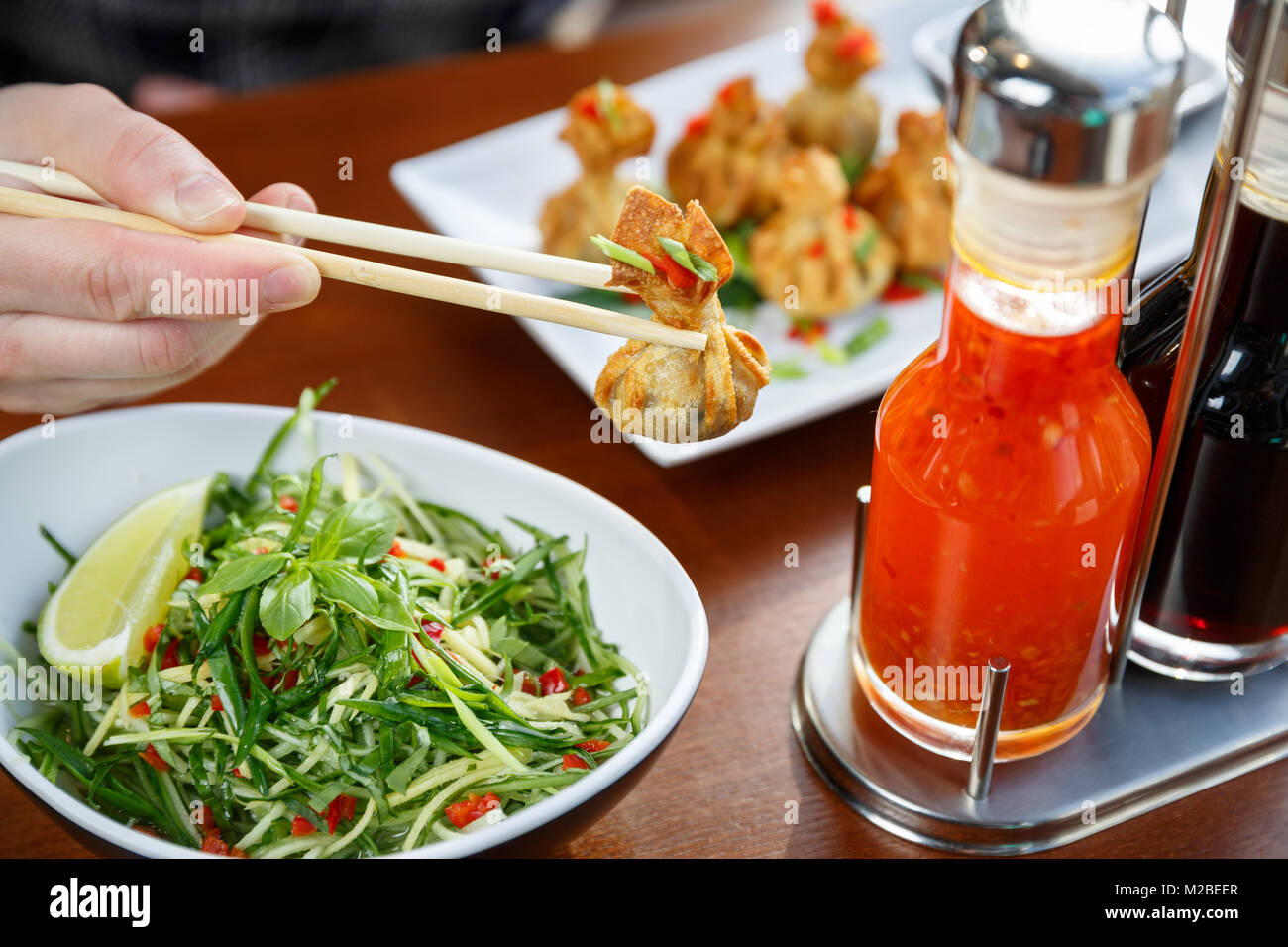 Main tenant un wonton frit avec des bâtons, avec salade de légumes et d'un ensemble de commandes sauses sur une table Banque D'Images