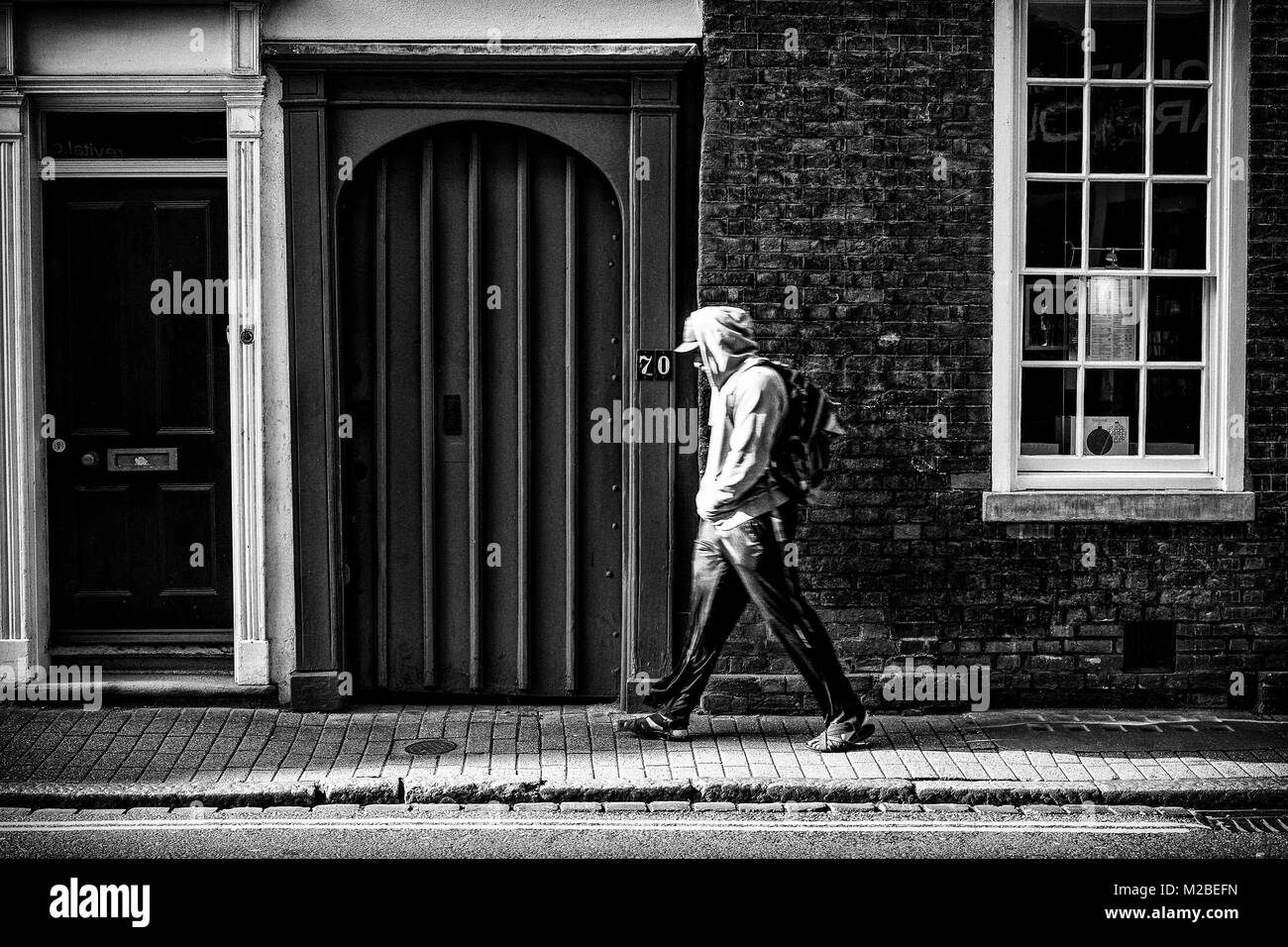 Teenage boy walking passé une porte à Cambridge. Tourné en noir et blanc Banque D'Images