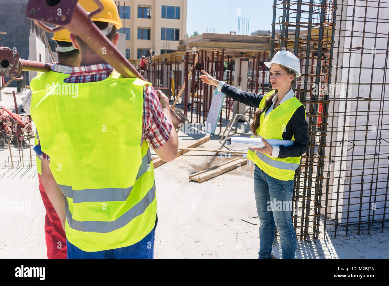 Contremaître expérimenté femme coordonner et de guider les travailleurs en leur montrant la bonne direction lors des travaux sur le site de construction d'un contemporain Banque D'Images