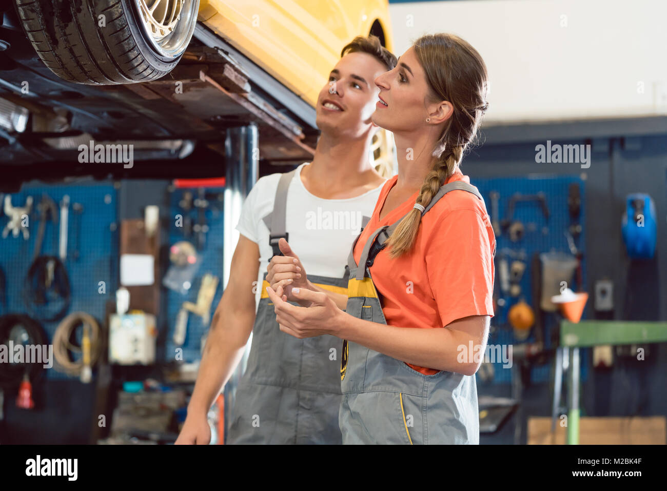 Deux mécaniciens auto smiling happy, lors de la vérification de la mise à roues d'une voiture à l'écoute après avoir travaillé ensemble dans une réparation automobile moderne sho Banque D'Images