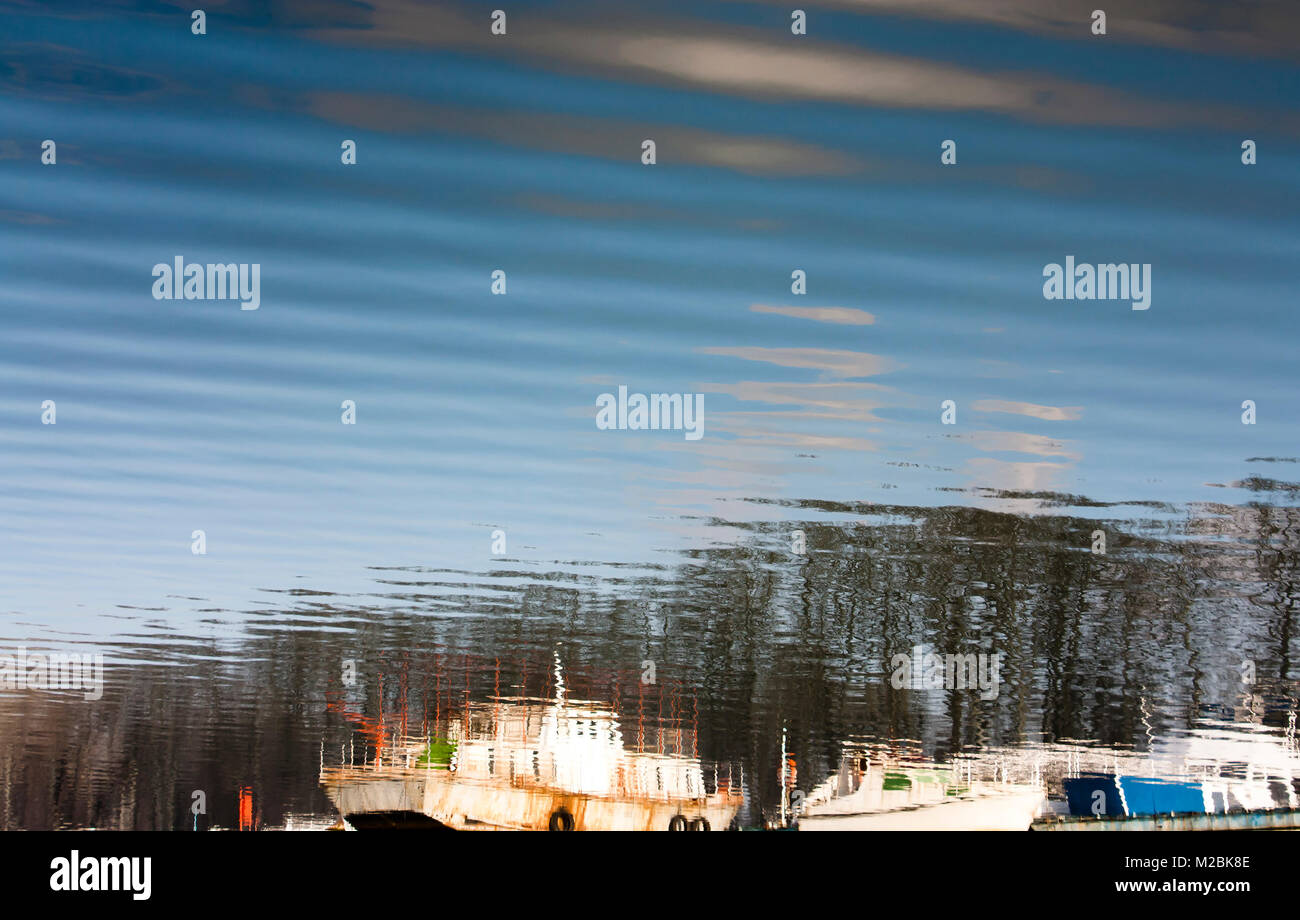 Réflexion floue de vieux bateaux ancrés, arbres, ciel bleu et nuages dans l'eau de la rivière Banque D'Images