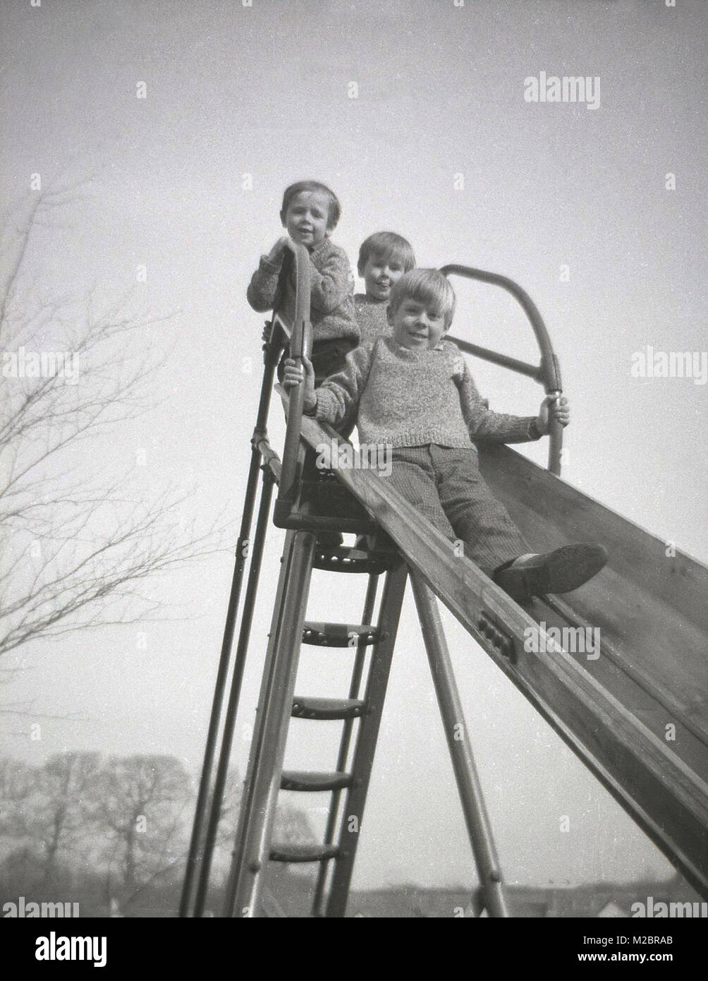 Années 1960, historiques, trois petits garçons ensemble, tous frères, et porter les mêmes étoffes cavaliers, regarder vers le bas du haut d'un metal aire de glisse, England, UK. Banque D'Images