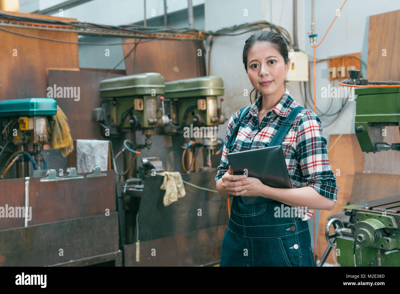 Joli sourire femme chef d'entreprise holding digital tablet mobile face à l'appareil photo lorsque elle debout dans machine-usine. Banque D'Images