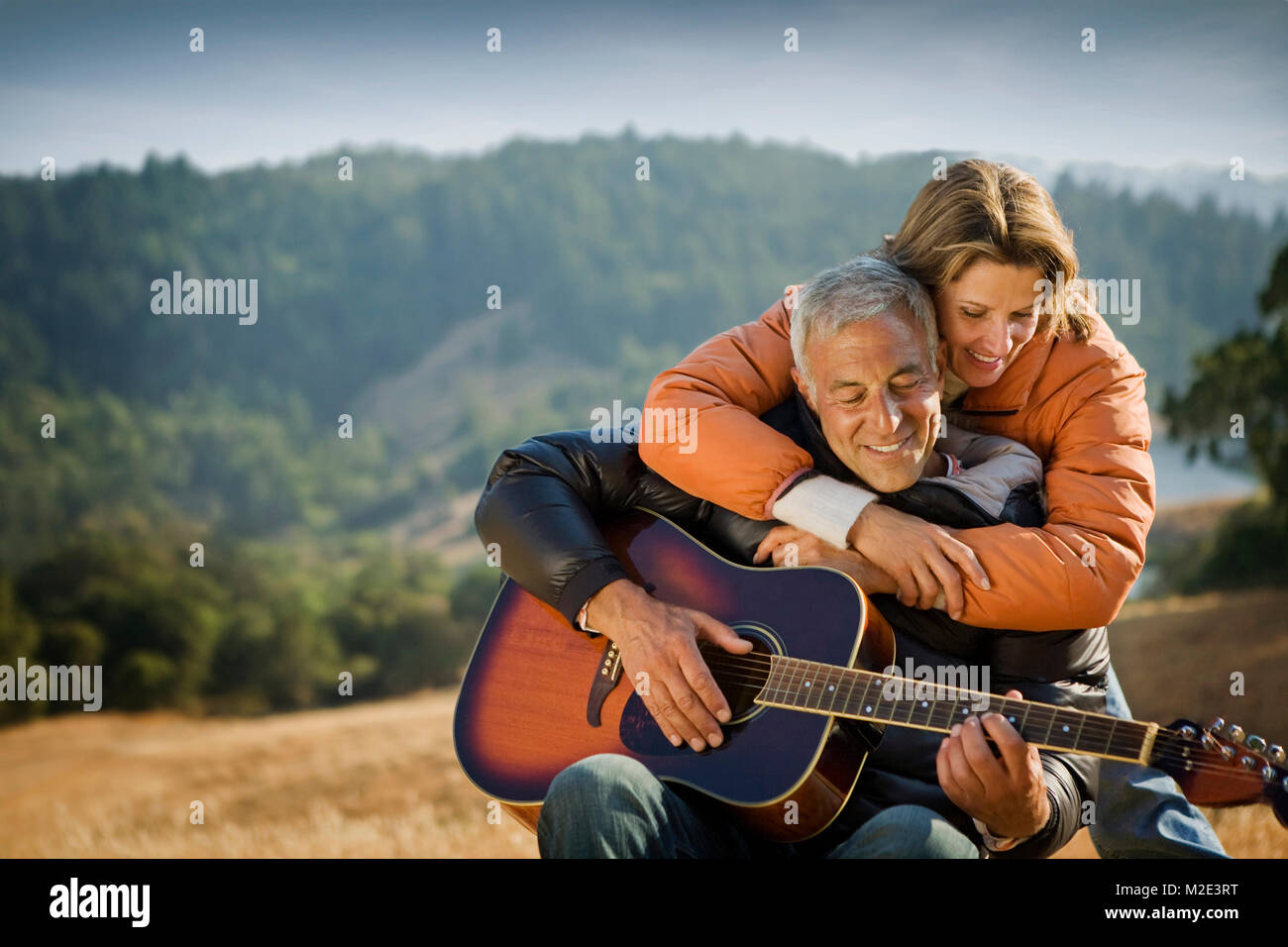 Woman hugging man playing guitar Banque D'Images