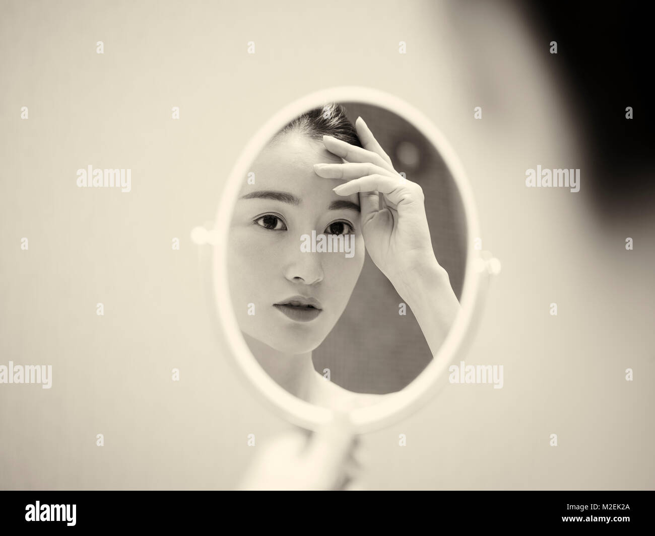 Belle jeune femme asiatique se voir dans le miroir, la main sur le front, noir et blanc, style rétro. Banque D'Images