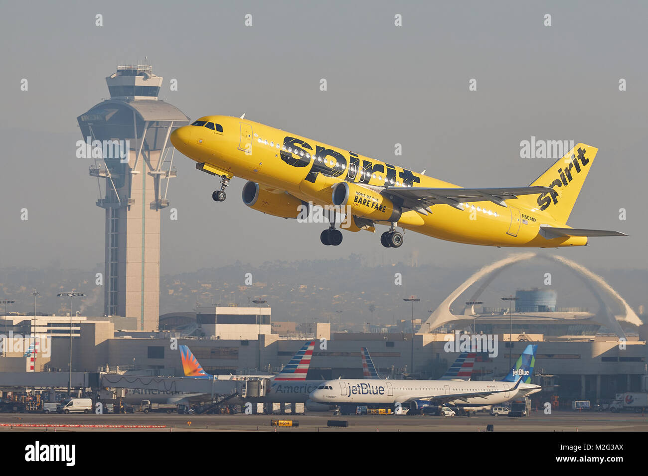 Spirit Airlines Airbus A320 jaune vif qui décollait de l'Aéroport International de Los Angeles, la tour de contrôle et le thème bâtiment derrière. Banque D'Images