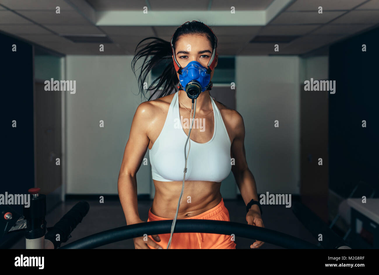 Portrait of female runner wearing mask on treadmill in sports science lab. Grande sportive s'exécutant sur un tapis roulant et le suivi de ses performances de remise en forme. Banque D'Images
