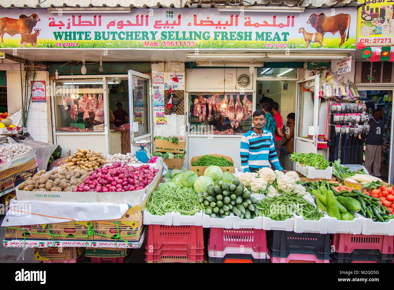 Un vendeur de légumes en face de son stand à un marché en plein air à Manama, Bahreïn, avec une boutique de la boucherie derrière Banque D'Images