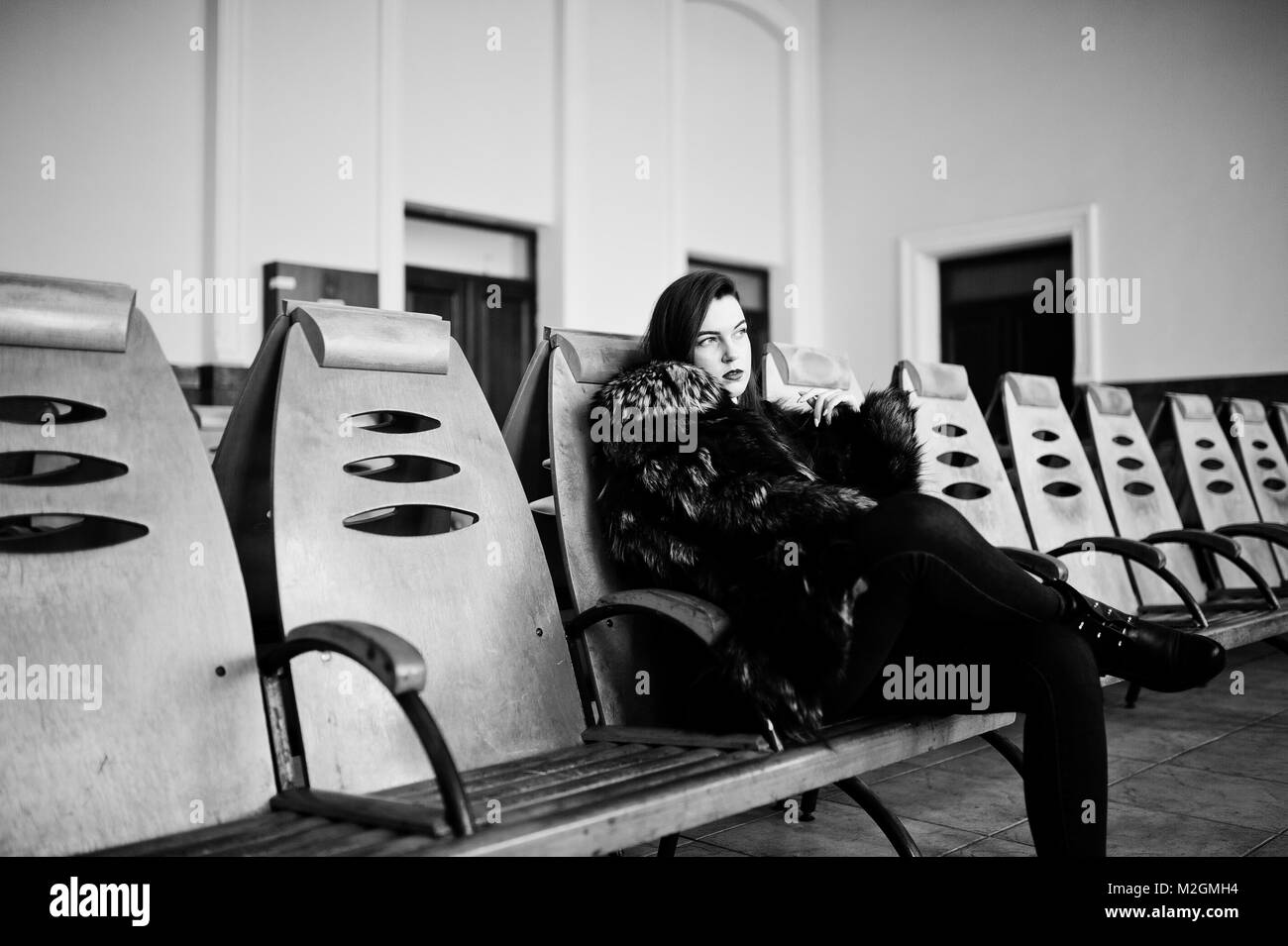 Brunette girl in green manteau de fourrure sur les chaises dans la salle d'attente à la gare. Banque D'Images