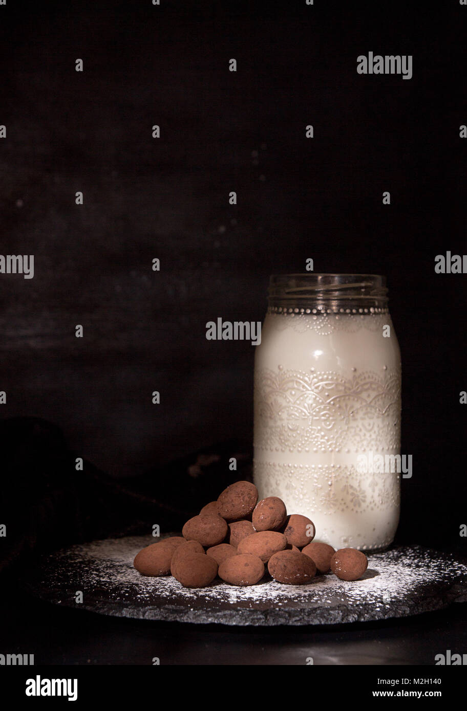 Bonbons amandes enrobée de chocolat pâte de cacao et verre de lait sur fond noir foncé. Copier l'espace. Banque D'Images