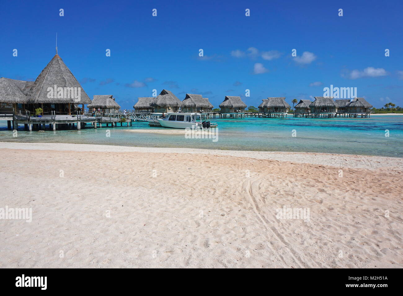 Tropical resort, plage de sable avec des bungalows au toit de chaume au-dessus de l'eau dans le lagon, l'atoll de Tikehau, Tuamotu, Polynésie Française, océan Pacifique, Océanie Banque D'Images