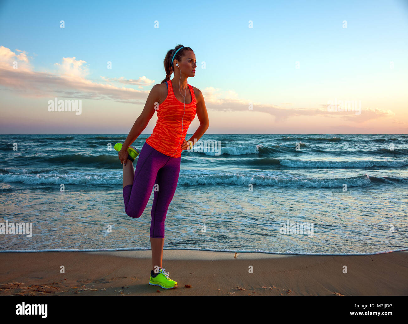 Côté mer sauvage rafraîchissante d'entraînement. Portrait de femme en fit de sport sur la plage au coucher du soleil s'étend Banque D'Images