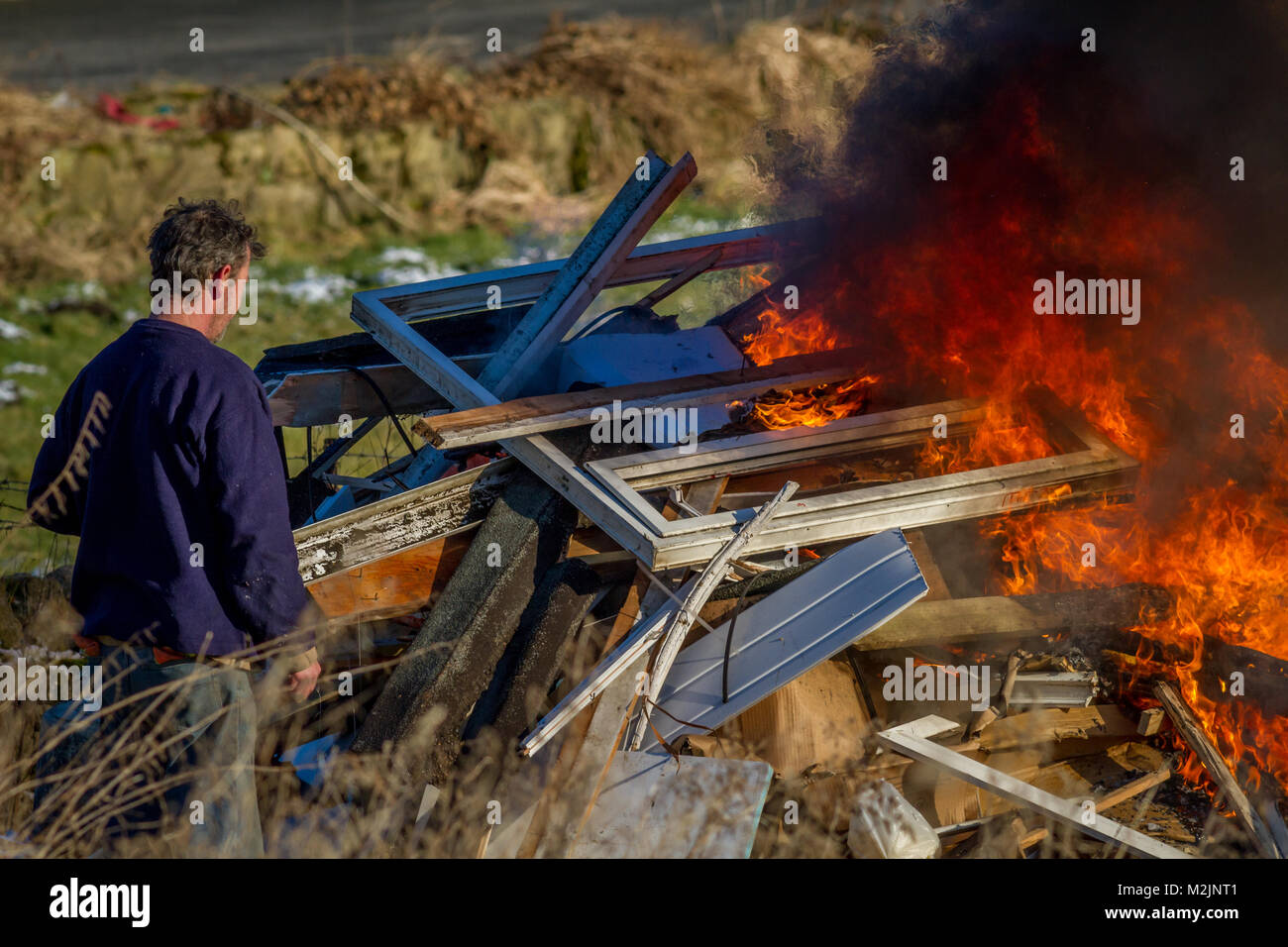 Personne au contrôle d'un feu brûlant des déchets d'une maison rénovation avec des flammes et de la fumée noire, probablement avec des fumées toxiques polluant l'environnement Banque D'Images