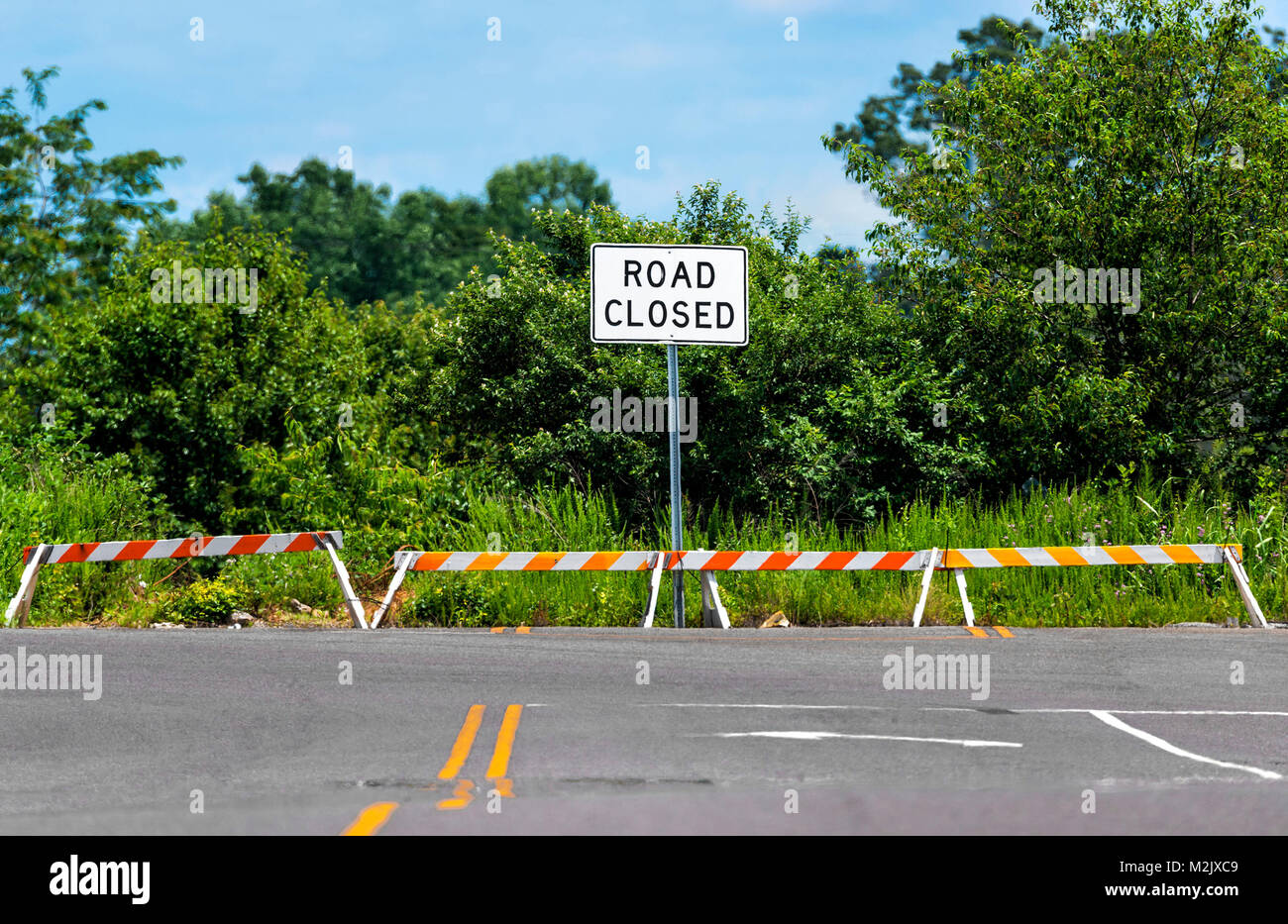 D'un coup horizontal road closed sign placé là où la route a pris fin. vert des arbres et arbustes derrière sous un ciel bleu. Banque D'Images