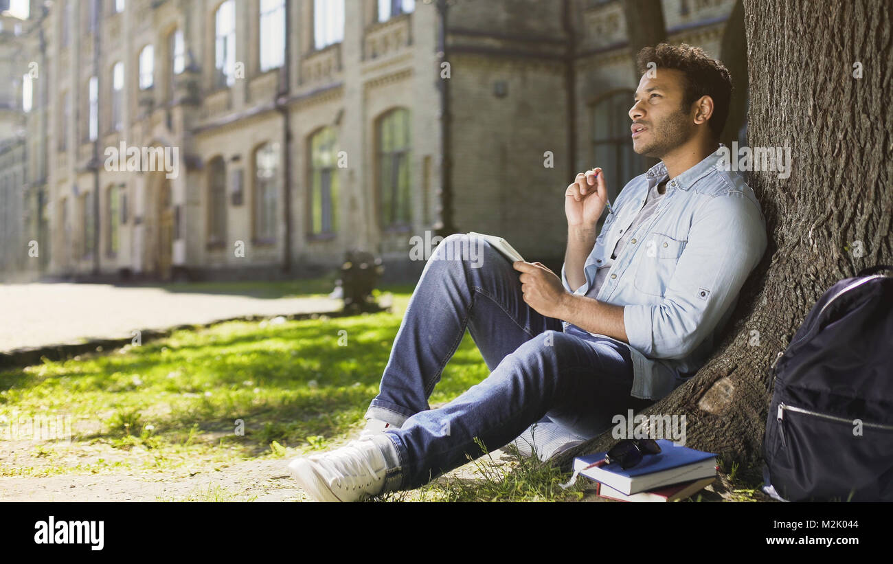 College student sitting with notebook en vertu de l'arbre faisant accueil perfectionnement, étudiant Banque D'Images