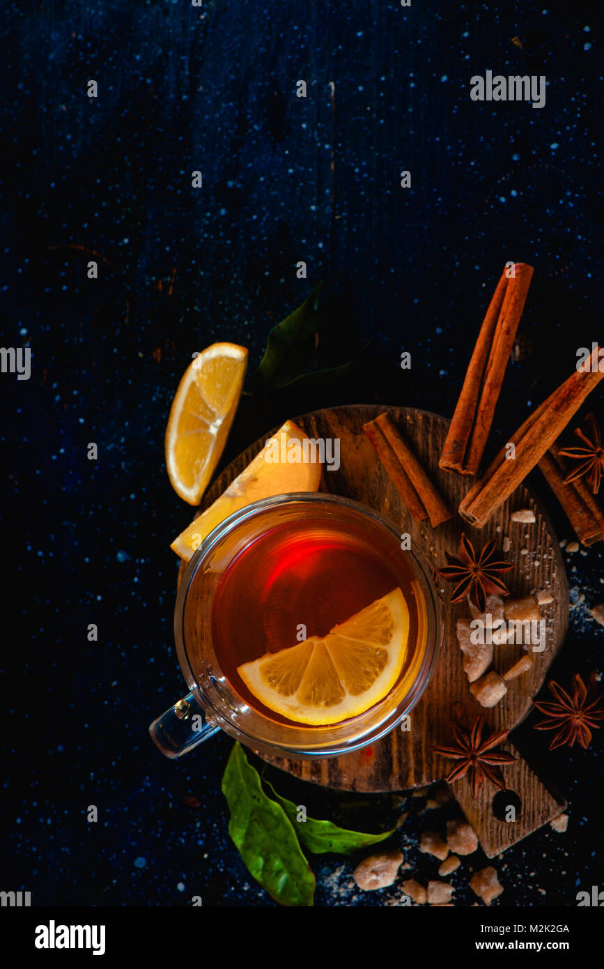 Thé au citron dans une double paroi en verre avec les tranches de citron, d'anis étoile, le sucre, les feuilles de thé et de cannelle sur un fond sombre. Boire de la photographie ci-dessus. Co Banque D'Images
