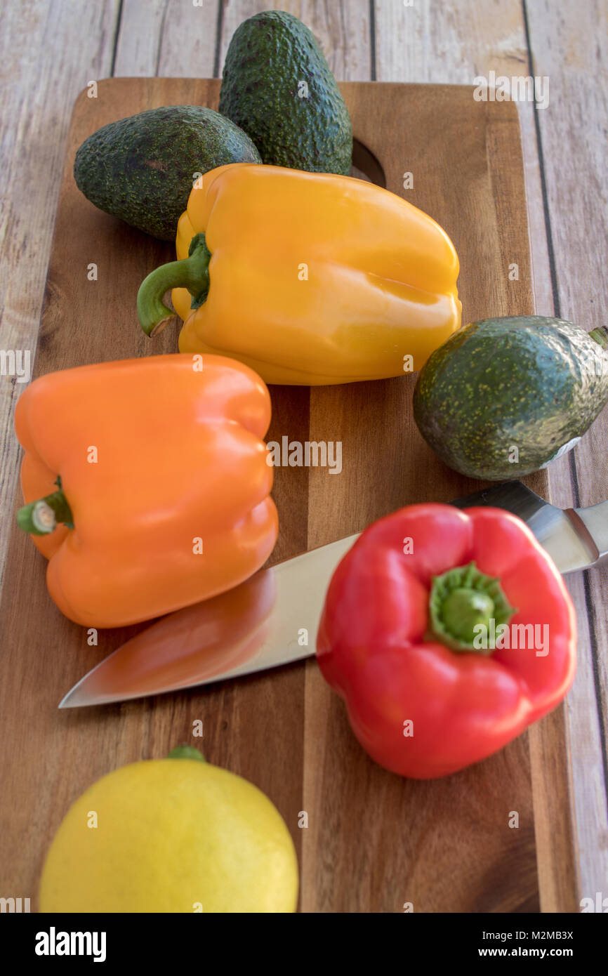 Les poivrons et d'avocat sur la planche à découper en bois Banque D'Images