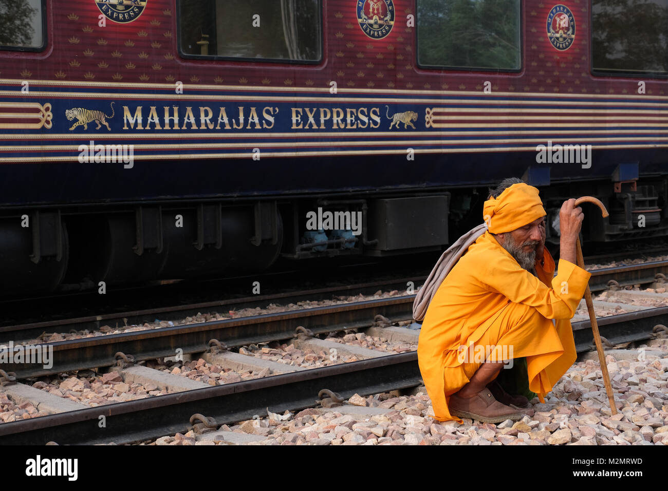 Un homme accroupi à côté du du Maharaja's Express, train touristique de luxe,Rajasthan, Inde Banque D'Images