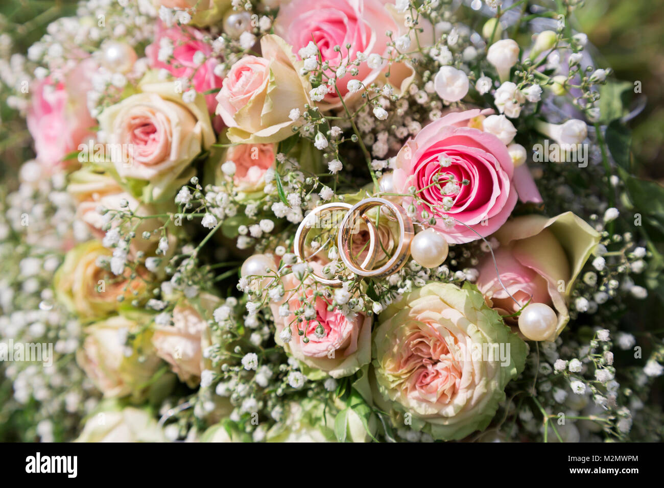 Close up of fresh romantique bouquet de mariage coloré de roses roses avec  de petites fleurs des champs sauvages blancs avec deux anneaux de mariée  mariée et le marié dans sunn Photo