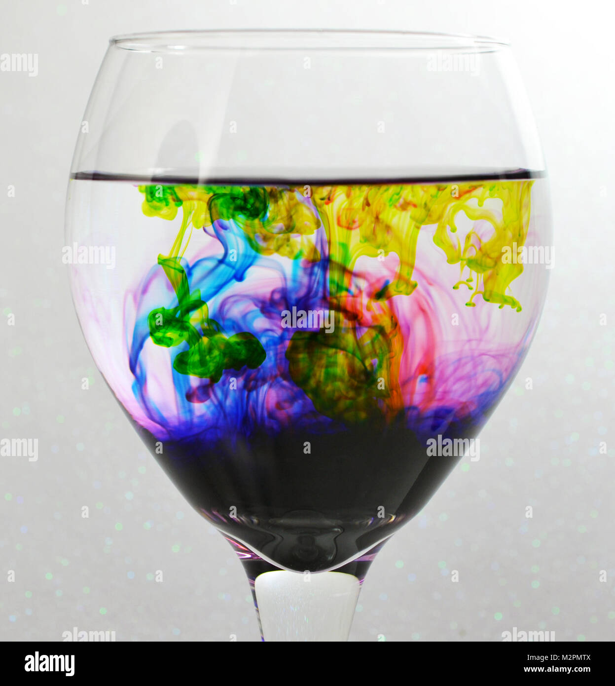 Verre de vin rempli d'eau et de vert, bleu, rouge et violet gouttes de colorant Banque D'Images