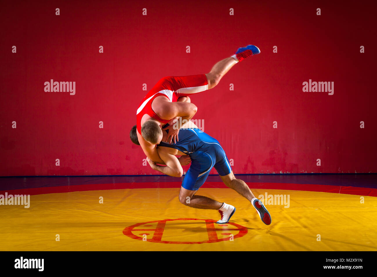 Deux jeunes hommes lutteurs dans le bleu et le rouge wrestling collants sont wrestlng et faire un jet de hanche sur un tapis de lutte jaune dans la salle de sport, sied voir Banque D'Images