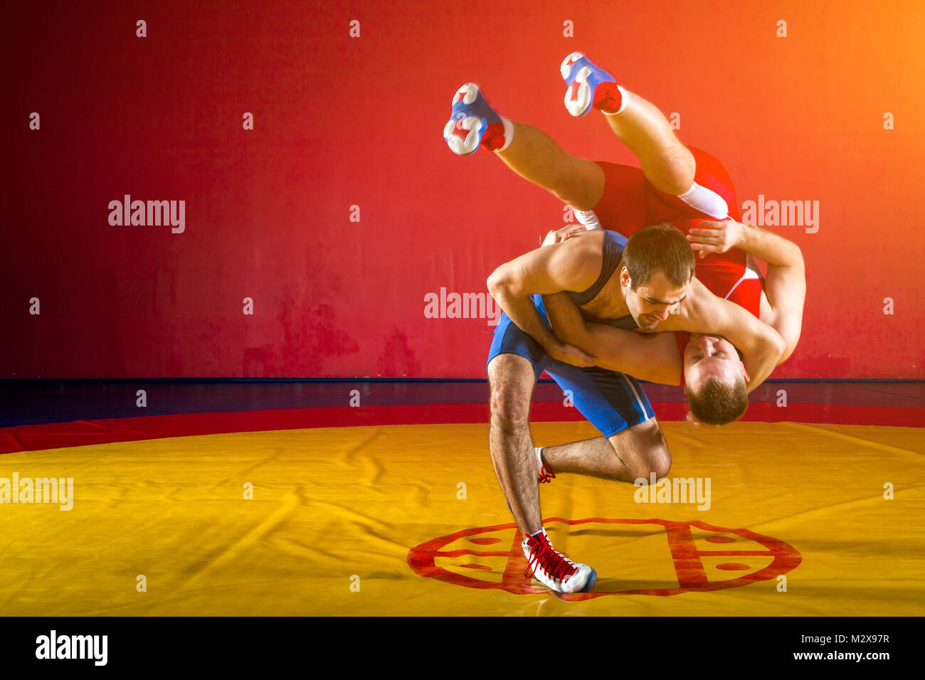 Deux jeunes hommes en bleu et rouge wrestling collants sont wrestlng et faire une suplex wrestling wrestling jaune sur un tapis dans la salle de sport Banque D'Images