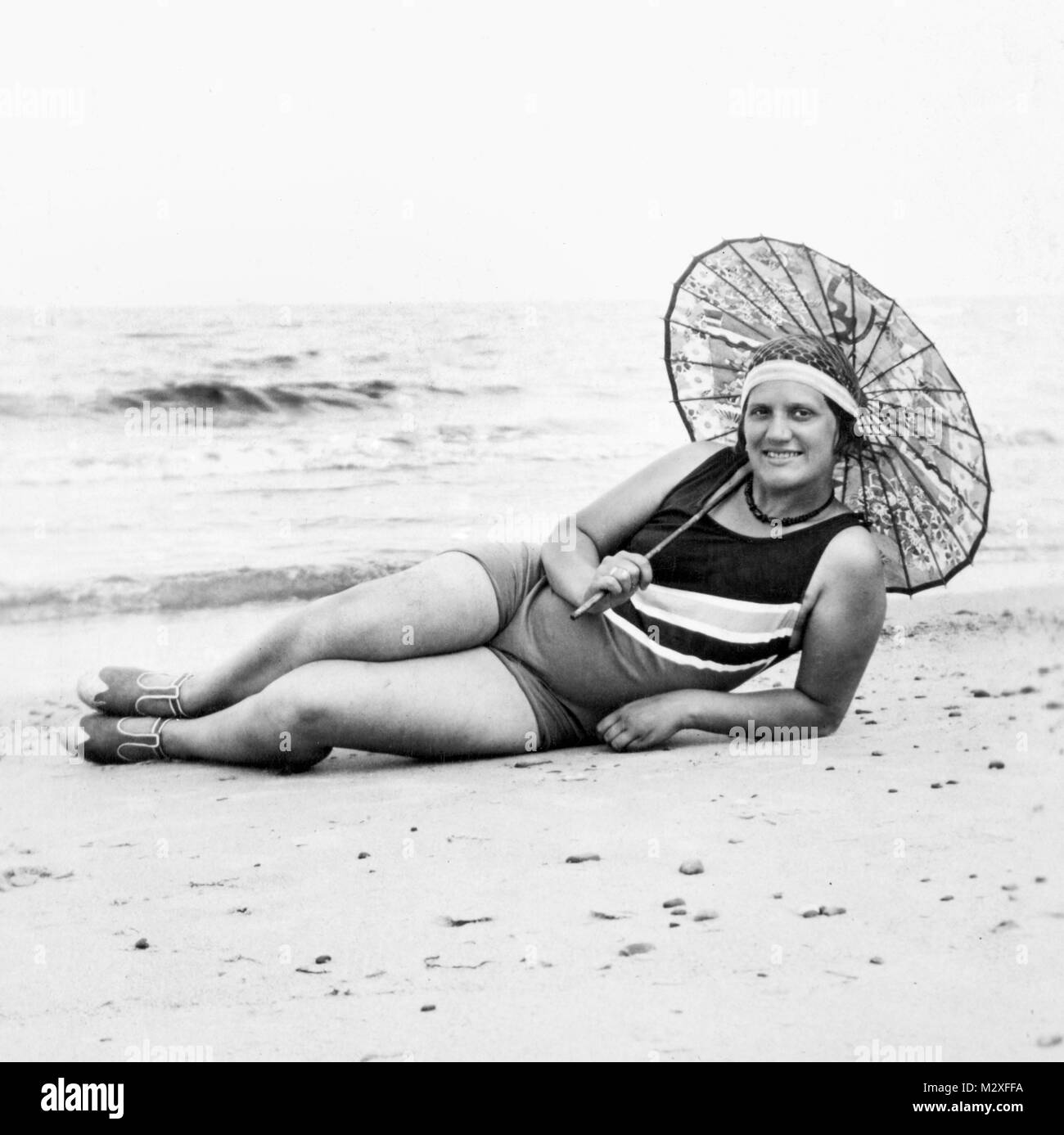 Jeune femme s'étend sur la plage avec son parapluie, ca. 1924. Banque D'Images