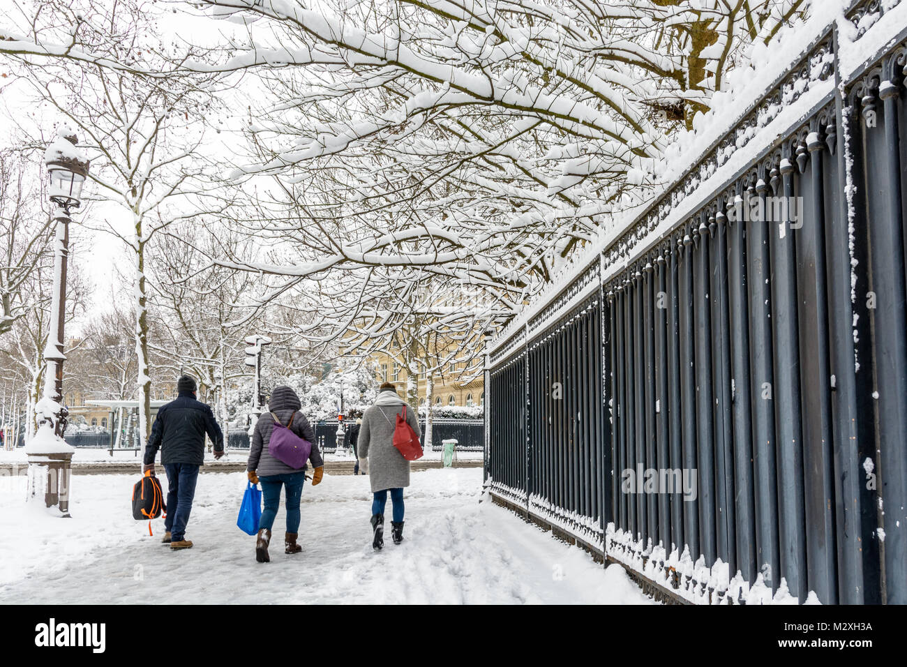 L'hiver à Paris dans la neige. Trois personnes enveloppé dans des vêtements chauds à pied sur un trottoir couvert de neige le long d'une haute silhouette noire clôture dans un quartier chic. Banque D'Images