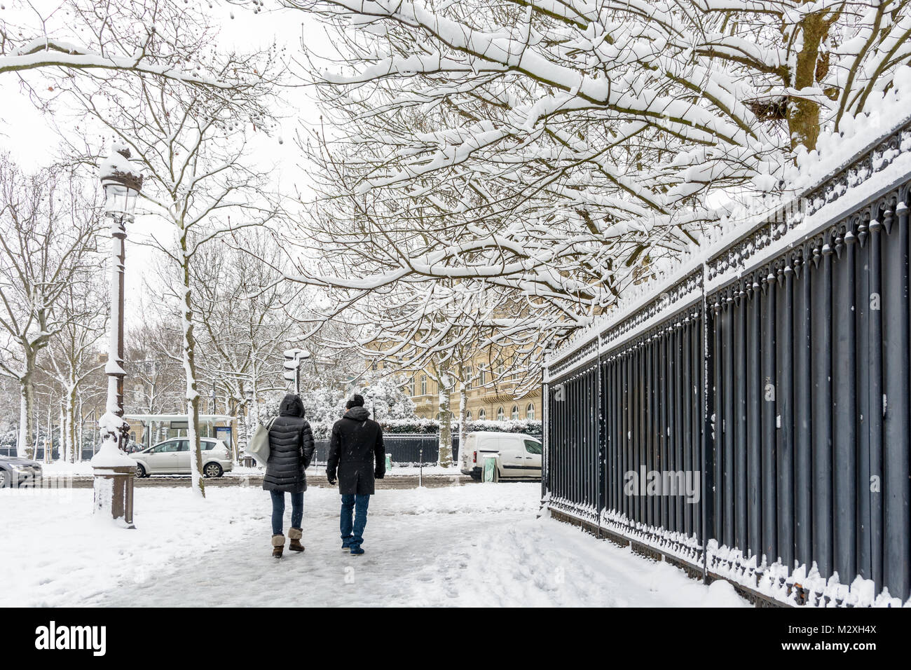 L'hiver à Paris dans la neige. Deux personnes enveloppé dans des vêtements chauds à pied sur un trottoir couvert de neige le long d'une haute silhouette noire clôture dans un quartier chic. Banque D'Images