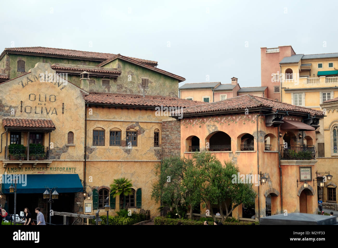 L'architecture de style Toscane Italie. Old Weathered bâtiments orange pâle, sol en terre cuite des toits. Restaurant avec auvent bleu. Quelques personnes à pied. Banque D'Images