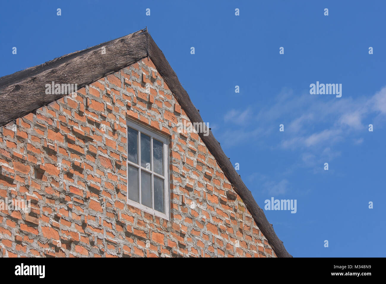 Fenêtre sur mur de brique brune et toiture en bois de style vintage avec fond de ciel bleu. Banque D'Images