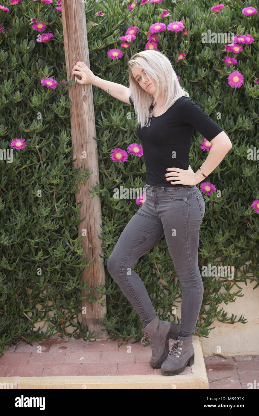 Belle fille blonde en jeans se leva d'un mur de fleurs Banque D'Images