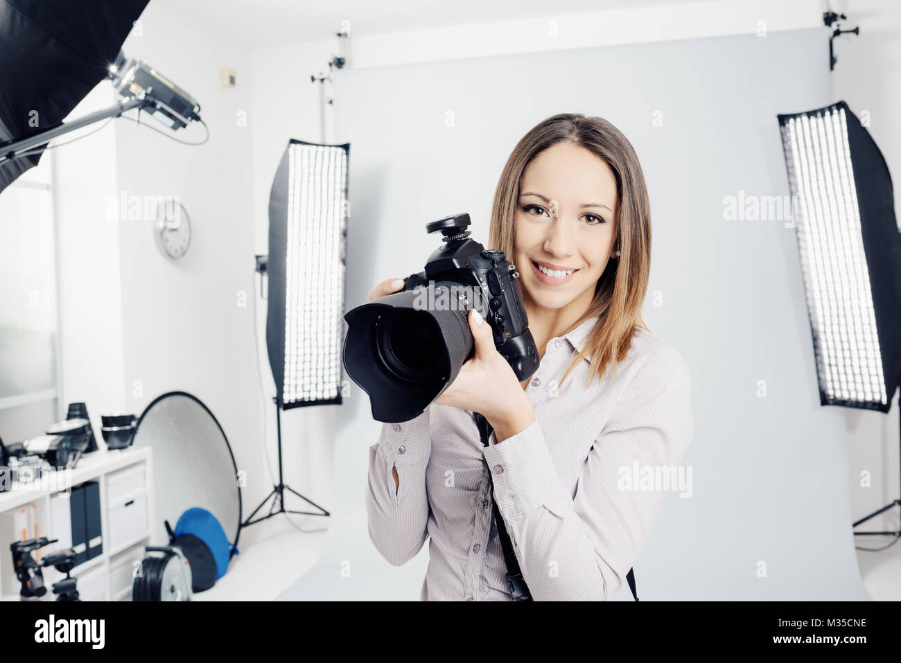 Jeune femme photographe posant dans le studio photo, il est souriant et tenant un appareil photo numérique professionnel Banque D'Images