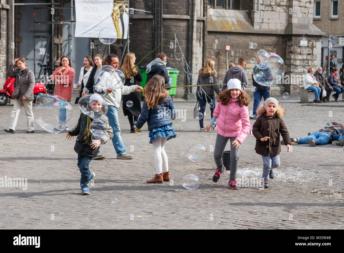 Enfants jouant et s'amusant avec les bulles de savon à la place Saint Nicolas sur une journée ensoleillée. Gand, Belgique. Banque D'Images