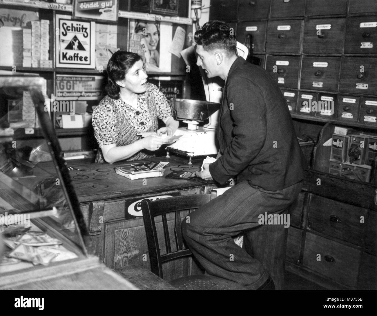 Un vendeur essaie d'expliquer les principales des bons alimentaires à un client qui a des doutes, à un magasin de marchandises coloniales à Heidelberg. Dans le monde d'utilisation | Banque D'Images